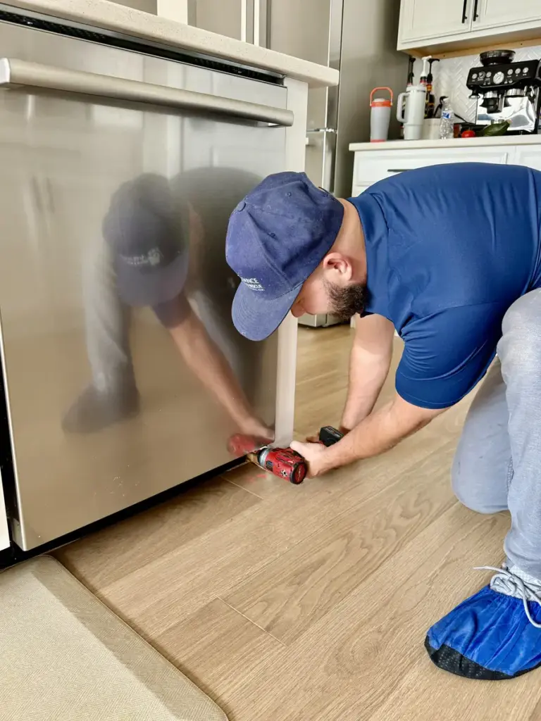 Appliance repair technician servicing a Bosch dishwasher with a cordless driver